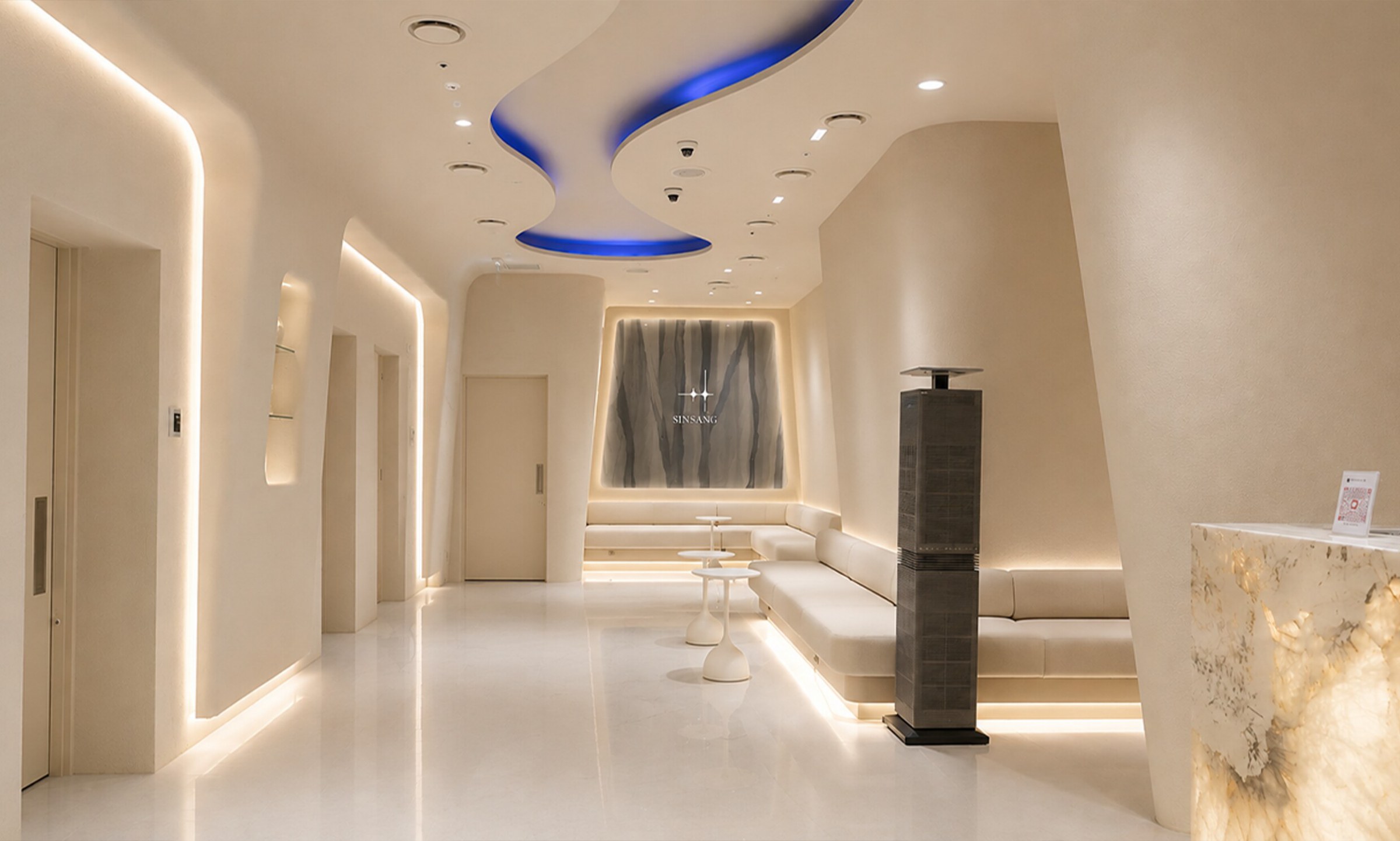 Hallway leading to a sofa lounge under a blue-lit ceiling